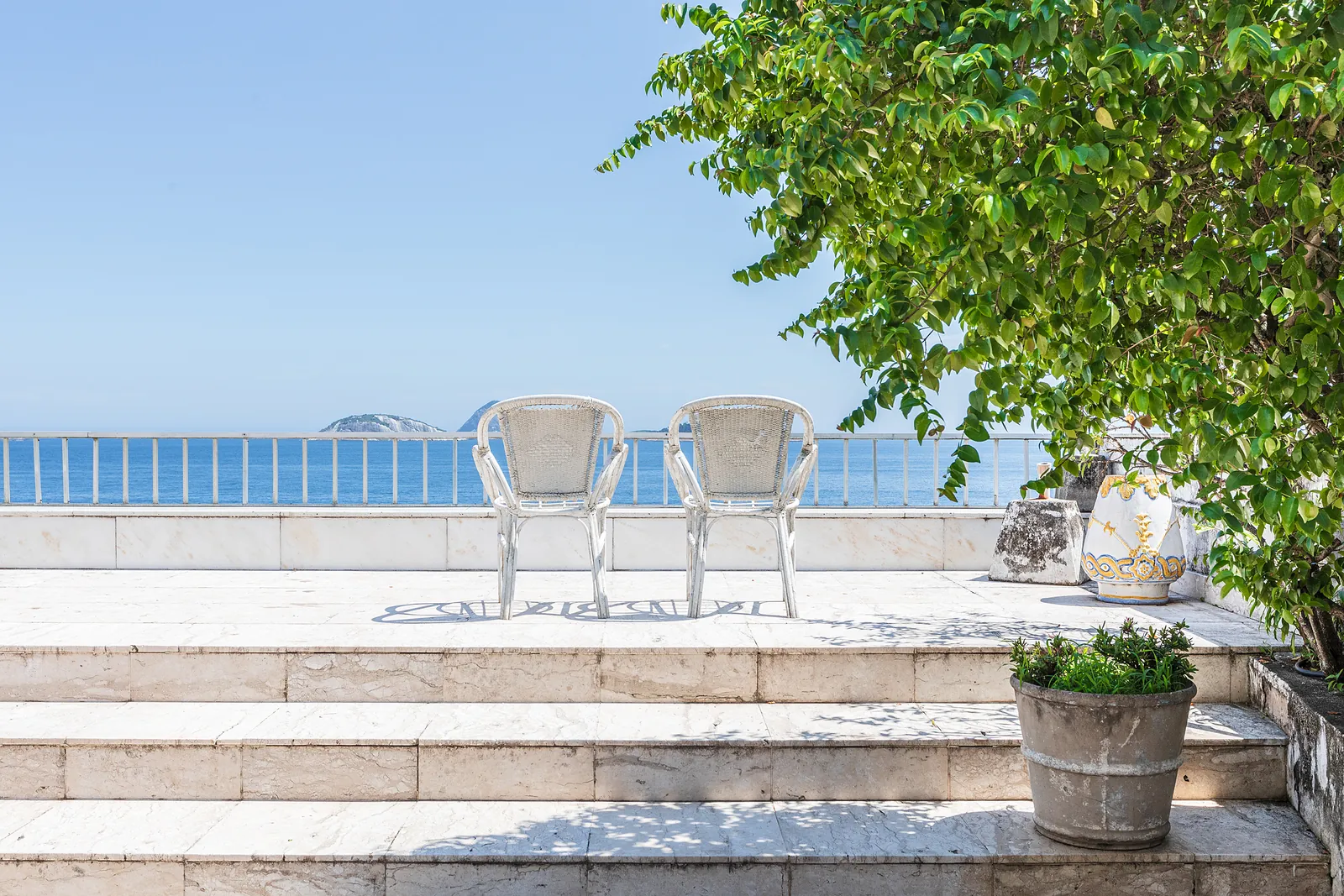 Une terrasse sur le toit avec un arbre, des chaises et la mer au fond